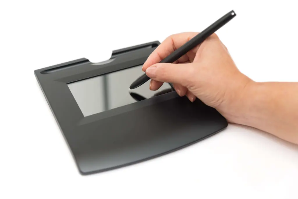Image showing the action of signing on a digitized signature pad. Hand holding a stylus and signing on the digital signature pad. 